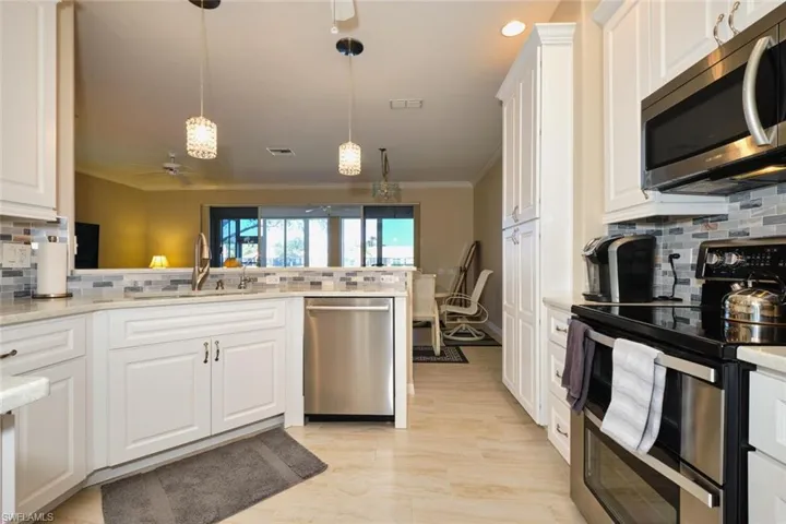 Kitchen with backsplash, stainless steel appliances, a ceiling fan, white cabinets, and crown molding