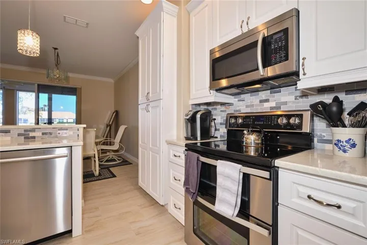 Kitchen with stainless steel appliances, light stone counters, hanging light fixtures, tasteful backsplash, and white cabinets