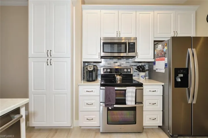 Kitchen featuring stainless steel appliances, white cabinetry, backsplash, and light stone countertops