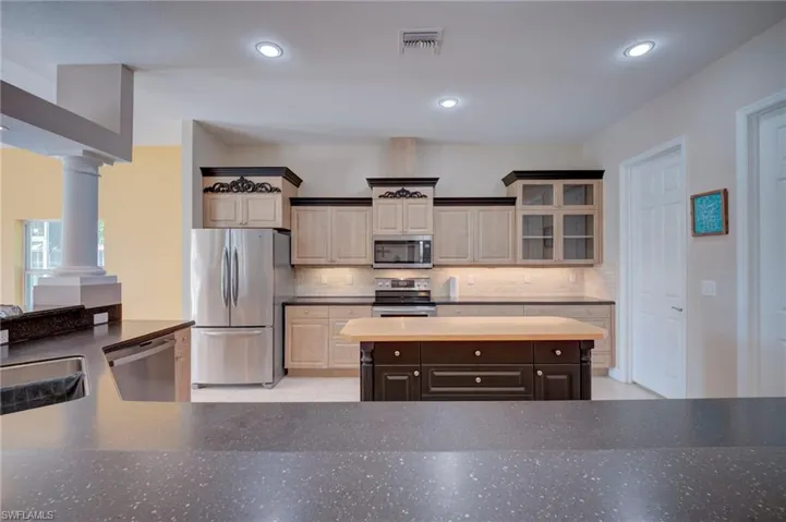 Kitchen featuring stainless steel appliances, a kitchen island, recessed lighting, glass insert cabinets, and tasteful backsplash