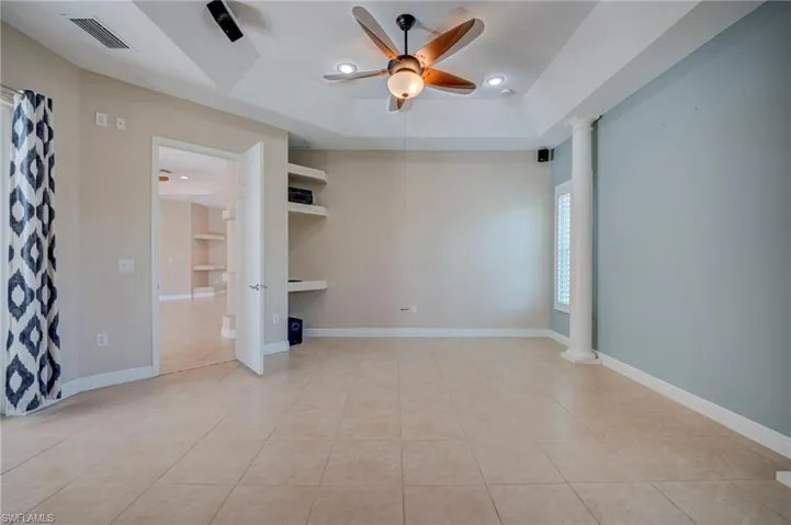 Spare room featuring ceiling fan, ornate columns, a tray ceiling, and light tile patterned floors