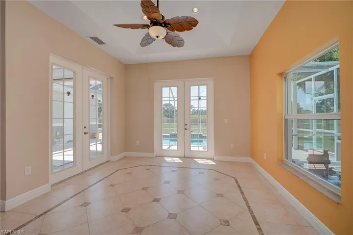 Empty room with french doors, a tray ceiling, inlaid floor details, and a ceiling fan