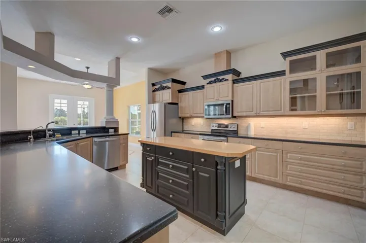 Dual tone kitchen featuring light tile patterned floors, glass insert cabinets, stainless steel appliances, ornate columns, and recessed lighting