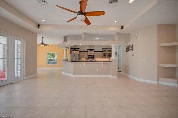 Unfurnished living room featuring ceiling fan, decorative columns, recessed lighting, and a tray ceiling