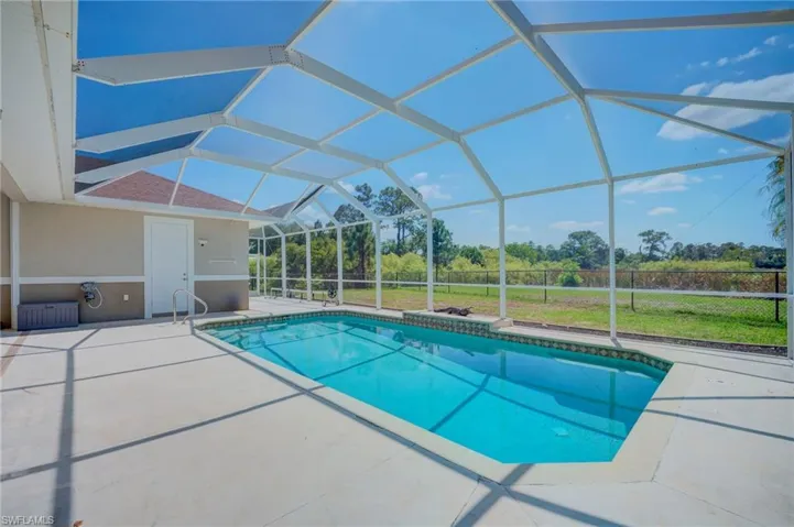Outdoor pool with a sunroom, a patio area, a yard, and glass enclosure