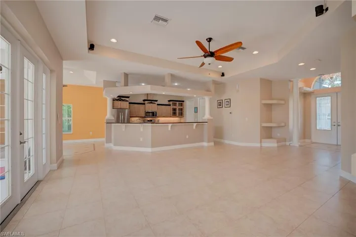 Unfurnished living room with french doors, a raised ceiling, ceiling fan, recessed lighting, and decorative columns
