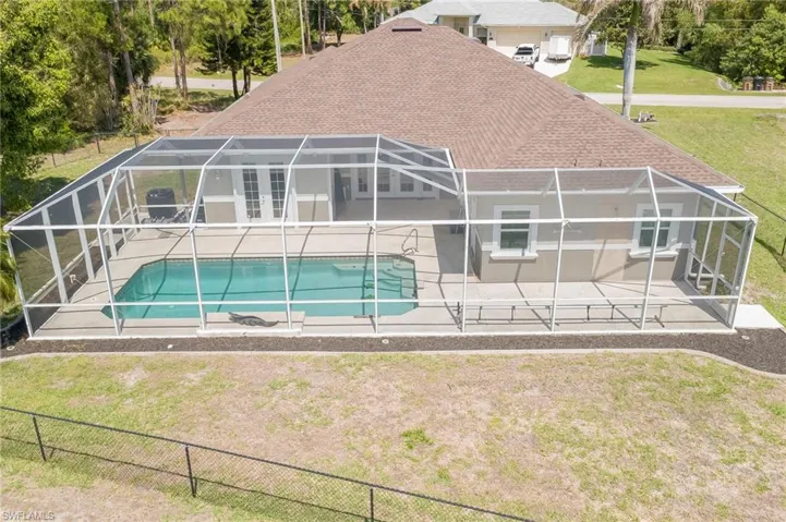 Rear view of property with a shingled roof, an outdoor pool, a lanai, a sunroom, and a lawn