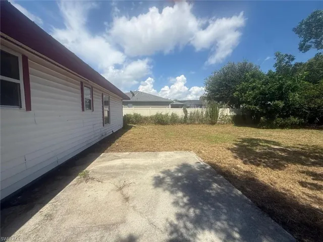 Expansive backyard with a concrete patio pad, mature trees, and a privacy fence