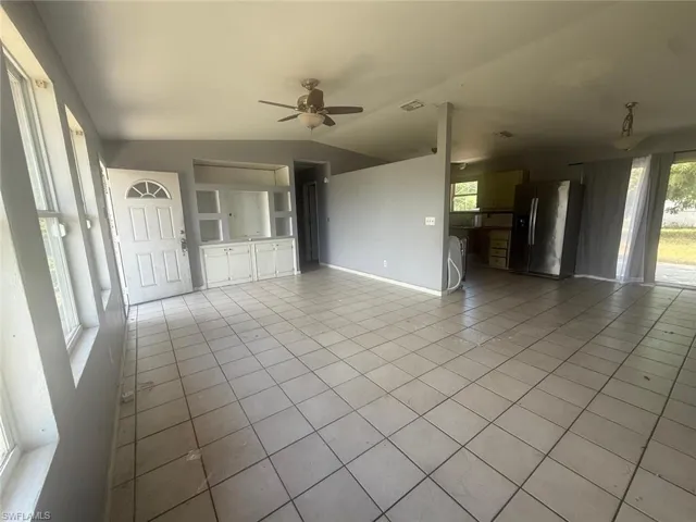 Open-concept living area featuring light-toned tile flooring, a white paneled front door, and a ceiling fan