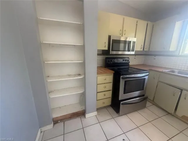 Kitchen featuring white tile flooring, wood-finish countertops, and a stainless steel oven with an overhead microwave