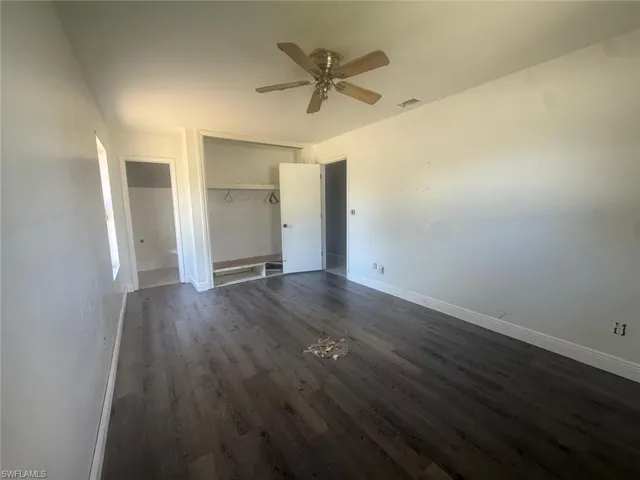 Room featuring dark wood-finish flooring, white walls, and a ceiling fan with brass accents