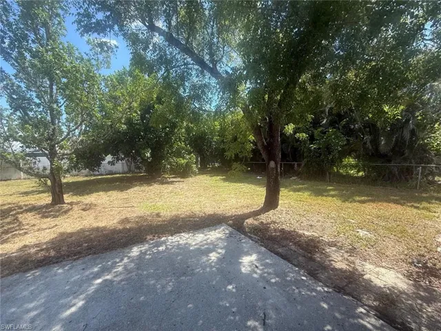 Expansive exterior space featuring established trees providing natural shading, a combination of concrete patio and natural ground cover, and a perimeter fence