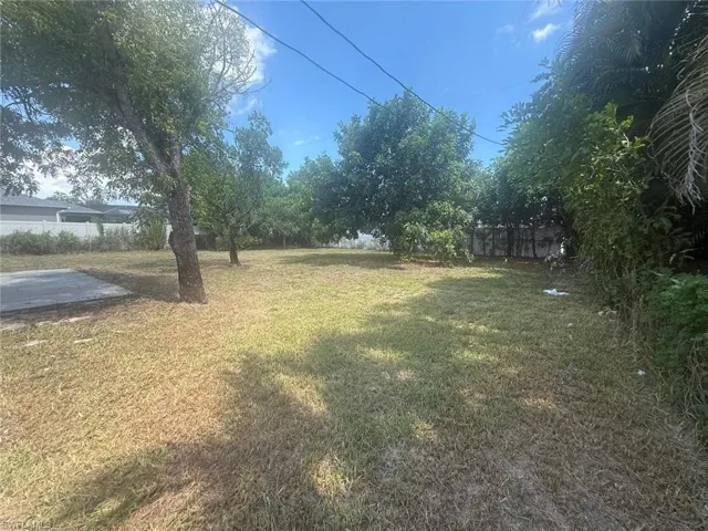 Expansive backyard featuring a large grass area, mature trees, and a concrete pad