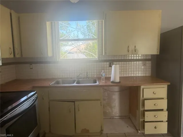 Kitchen featuring a double basin stainless steel sink, wood-finish countertops, tiled backsplash, upper and lower cabinetry, and an integrated four-drawer unit