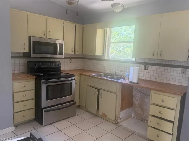 Kitchen featuring wood-finish countertops, light-toned cabinetry, stainless steel microwave, electric range, and a double basin sink