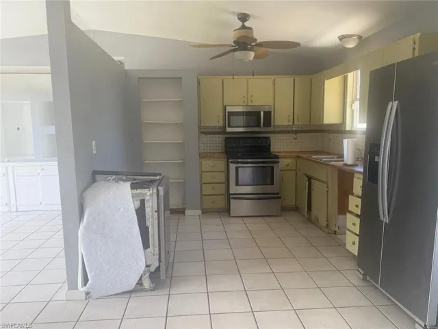 Kitchen featuring light-colored tile flooring, built-in shelving, stainless steel appliances, and a ceiling fan