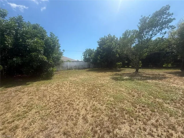 Expansive outdoor space featuring a large lawn area, mature trees providing natural shading, and a privacy fence enclosing the perimeter
