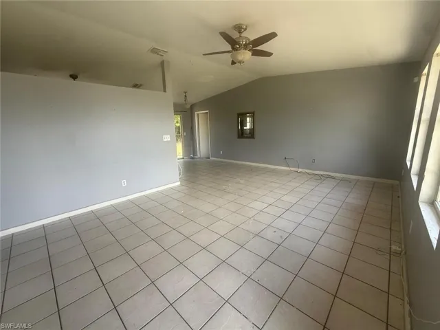 Spacious interior room featuring light-colored tile flooring, vaulted ceilings, and a ceiling fan with light fixture