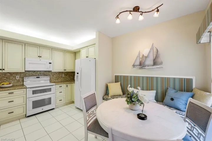 Kitchen with cream cabinets, white appliances, light tile patterned flooring, and light stone counters