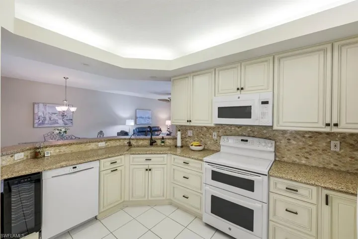 Kitchen with cream cabinetry, white appliances, light stone countertops, a chandelier, and tasteful backsplash
