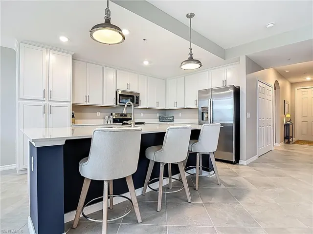 Kitchen with stainless steel appliances, light countertops, a center island with sink, white cabinets, and hanging light fixtures