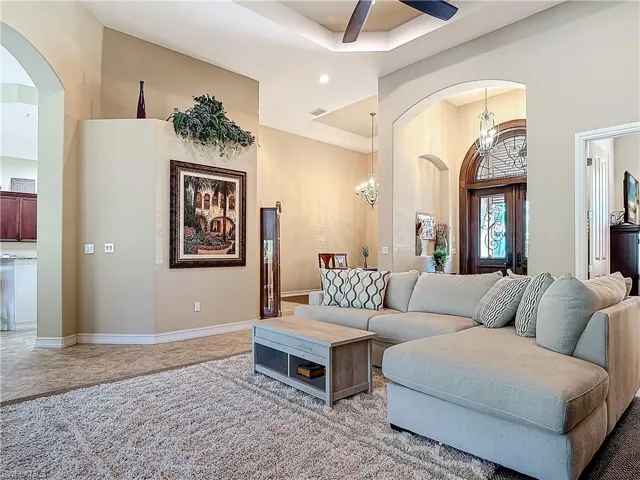 Living room featuring arched walkways, a tray ceiling, visible vents, baseboards, and ceiling fan with notable chandelier