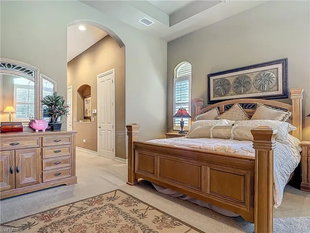 Bedroom with light colored carpet, arched walkways, and visible vents