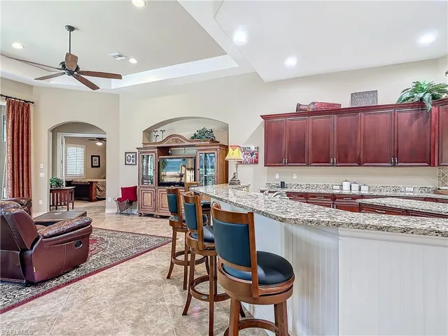 Kitchen featuring arched walkways, light stone counters, a ceiling fan, open floor plan, and reddish brown cabinets