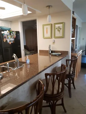 Pre Ian Kitchen with black fridge, hanging light fixtures, tile floors, dark stone counters, and sink