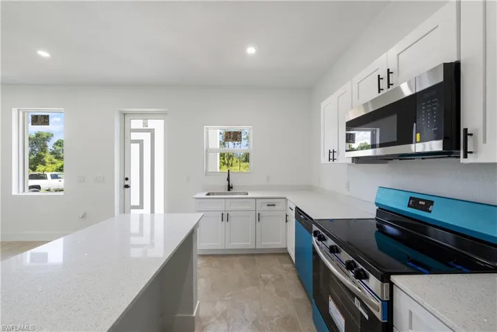 Kitchen with stainless steel appliances, white cabinets, light stone counters, and recessed lighting