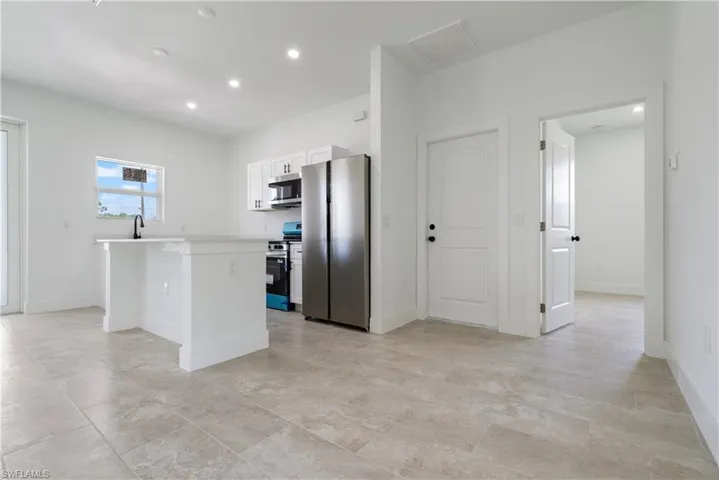 Kitchen with stainless steel appliances, a kitchen island, light countertops, white cabinetry, and recessed lighting