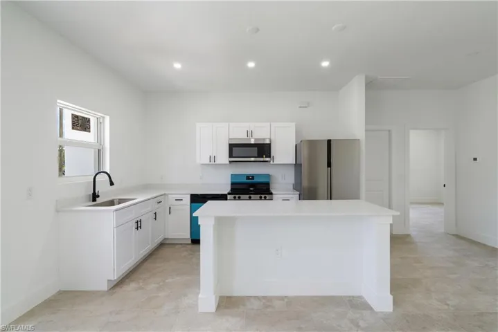Kitchen with stainless steel appliances, white cabinetry, a kitchen island, recessed lighting, and light stone counters
