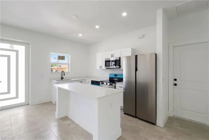 Kitchen with stainless steel appliances, a kitchen island, white cabinetry, recessed lighting, and light stone countertops