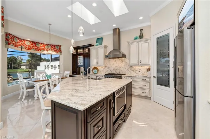 Kitchen with wall chimney range hood, cream cabinets, ornamental molding, and stainless steel appliances