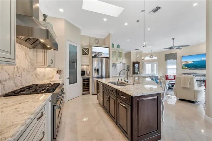 Kitchen with dark brown cabinetry, wall chimney exhaust hood, hanging light fixtures, sink, and appliances with stainless steel finishes