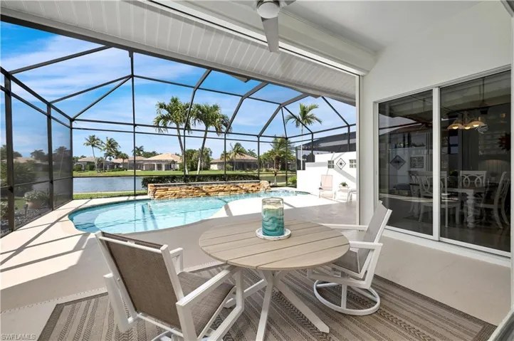 View of pool with glass enclosure, a patio area, a water view, and pool water feature