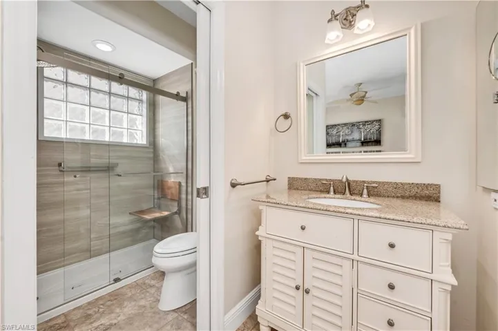 Bathroom featuring toilet, tile patterned flooring, vanity, ceiling fan, and a shower with shower door