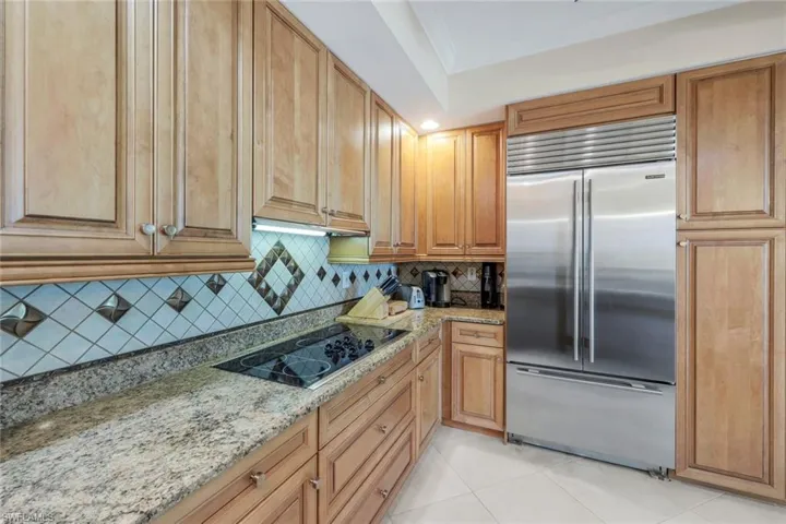 Kitchen with light stone countertops, black electric stovetop, tasteful backsplash, stainless steel built in fridge, and light tile floors