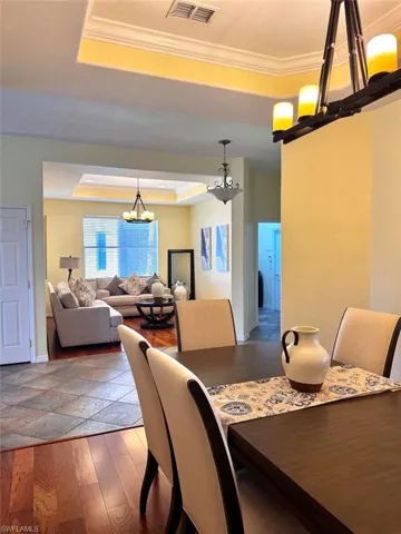Dining room featuring crown molding, dark wood-type flooring, a chandelier, and a tray ceiling