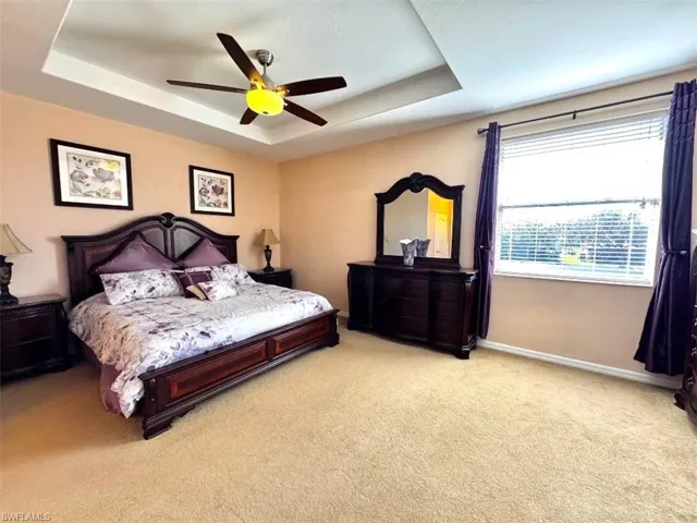 Carpeted bedroom with ceiling fan and a tray ceiling