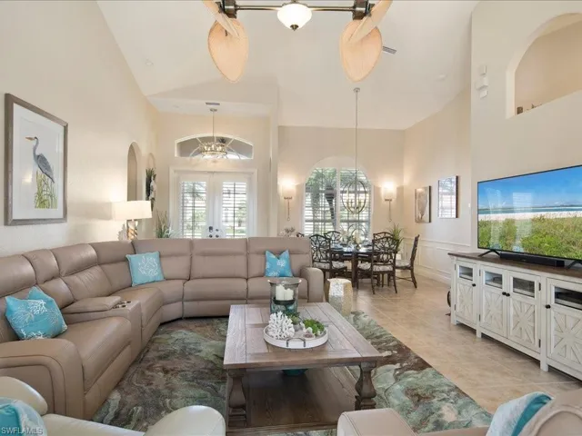 Living room featuring high vaulted ceiling, ceiling fan with notable chandelier, light tile patterned floors, and french doors