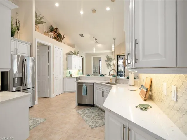 Kitchen with pendant lighting, stainless steel appliances, sink, vaulted ceiling, and white cabinets