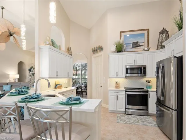 Kitchen featuring light tile patterned floors, stainless steel appliances, kitchen peninsula, high vaulted ceiling, and decorative backsplash