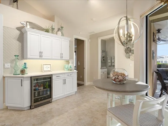 Kitchen with beverage cooler, white cabinets, lofted ceiling, and an inviting chandelier