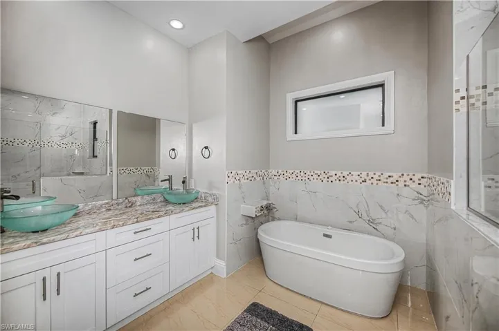 Full bath featuring a freestanding, soaking  tub, double vanity, tile walls, light marble finish floors, and a marble finish shower