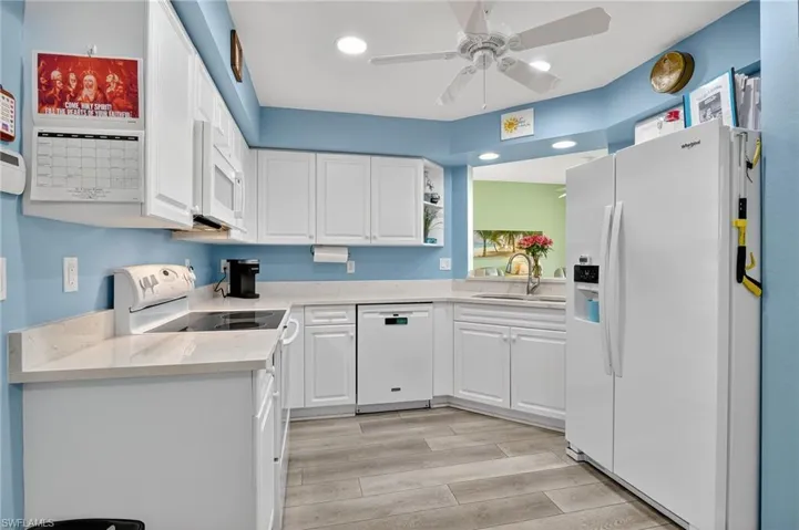 Kitchen with white appliances, white cabinetry, light wood-style flooring, ceiling fan, and recessed lighting