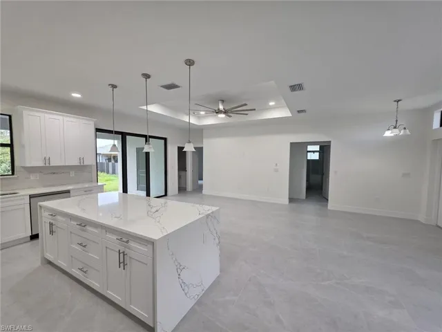 Kitchen with a tray ceiling, open floor plan, white cabinetry, a kitchen island, and dishwasher