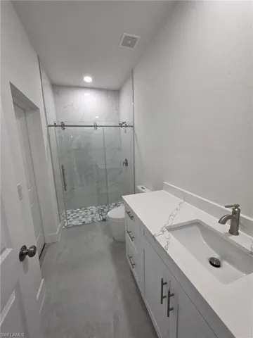 Bathroom featuring a marble finish shower, recessed lighting, visible vents, toilet, and vanity