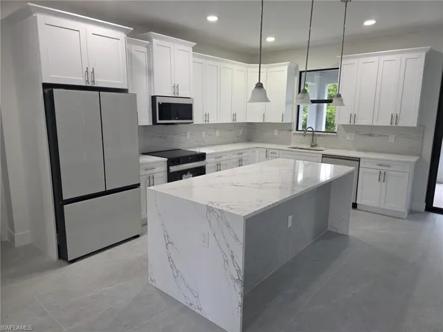 Kitchen with white cabinets, pendant lighting, stainless steel appliances, and a center island