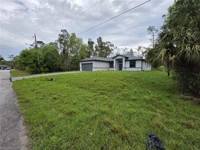 View of front of house with a garage, driveway, a front lawn, and stucco siding